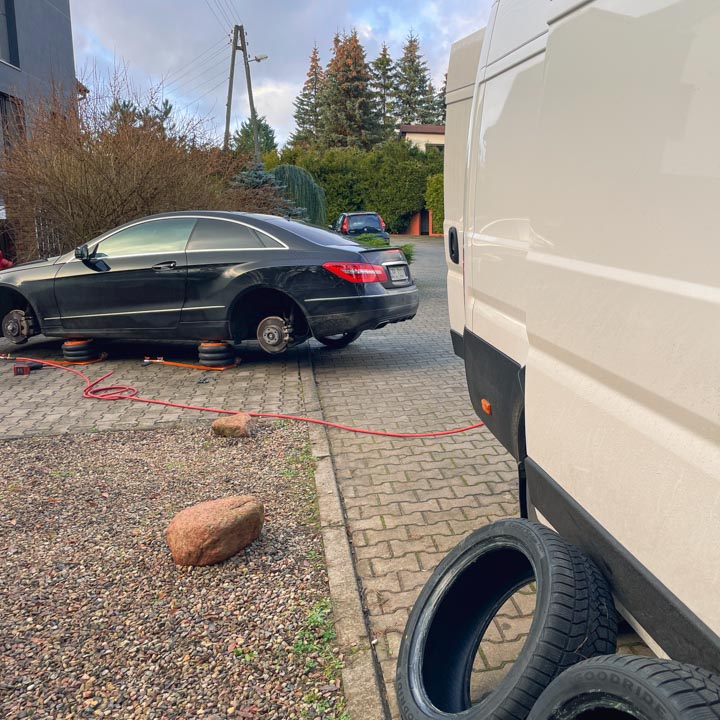 Czarny samochód marki Mercedes na dwóch podnośnikach pneumatycznych w trakcie wymiany opon