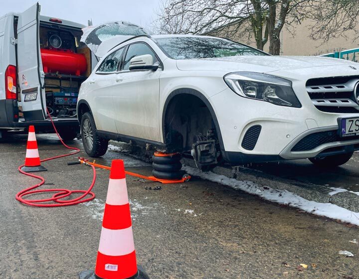 Mobilna wulkanizacja naprawia przebitą oponę w białym samochodzie marki Mercedes