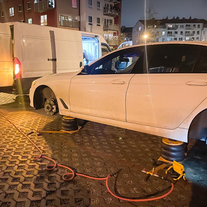Mobilna wulkanizacja wymienia opony na zimowe w białym samochodzie marki BMW pod domem klienta w godzinach wieczornych