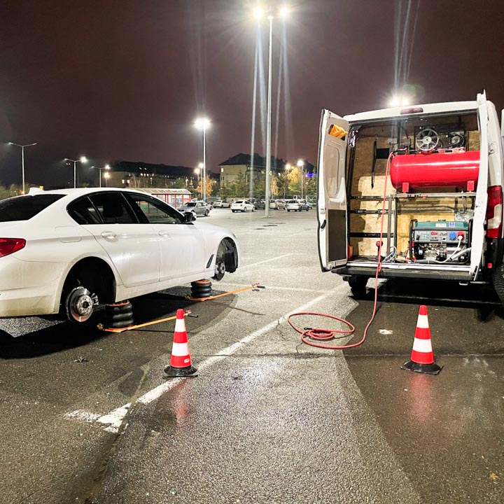 Mobilna wulkanizacja wymienia opony na zimowe w białym samochodzie marki BMW na parkingu centrum handlowego w nocy